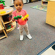 Riyah joined the competition — help win amazing prizes! toddler, child, toy, playroom, carpet, furniture, chair, table, pink_shirt, patterned_pants, white_shoes, hair_bows, puffs, indoor, colorful, early_learning, play, floor_mat, storage_shelves, curious