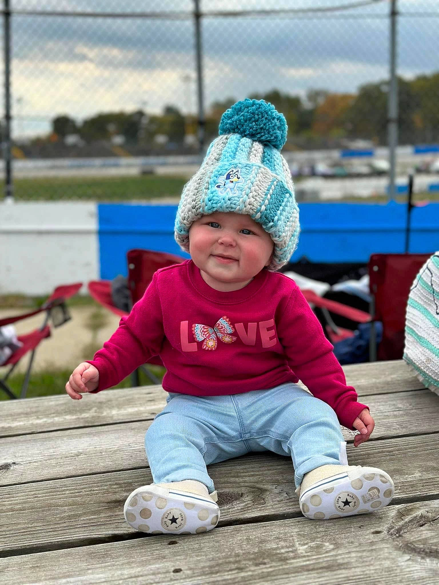 Clementine is registered to the contest to win money with this photo: baby, beanie, cap, child, city, electric_blue, fence, fun, grass, happy, headgear, headwear, joy, knit_cap, leisure, person, play, recreation, sitting, sky