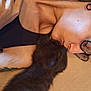 Artemis joined the competition — help win amazing prizes! person, kitten, black_cat, glasses, tattoo, close_up, affection, lying_down, kiss, pet, indoor, skin, hair, sleepy, gentle, love, soft_light, cozy, resting, cuddle