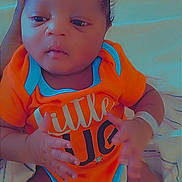 Dimitri is registered to the contest to win money with this photo: baby, infant, onesie, orange_clothing, blue_trim, blanket, hand, person, newborn, lying_down, cute, soft_lighting, indoors, sleepwear, child, face, skin, expression, small_hands, supporting_hand
