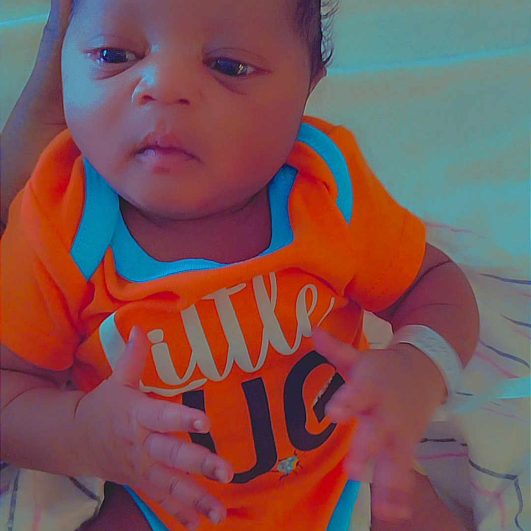 Dimitri is registered to the contest to win money with this photo: baby, blanket, blue_trim, child, cute, expression, face, hand, indoors, infant, lying_down, newborn, onesie, orange_clothing, person, skin, sleepwear, small_hands, soft_lighting, supporting_hand