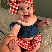 Gracelynn is registered to the contest to win money with this photo: baby, bed, blue_top, bow, cheerful, child, clothing, cute, hand_holding, happy, headwear, indoors, infant, person, portrait, quilt, red_and_white, sitting, skin, smiling