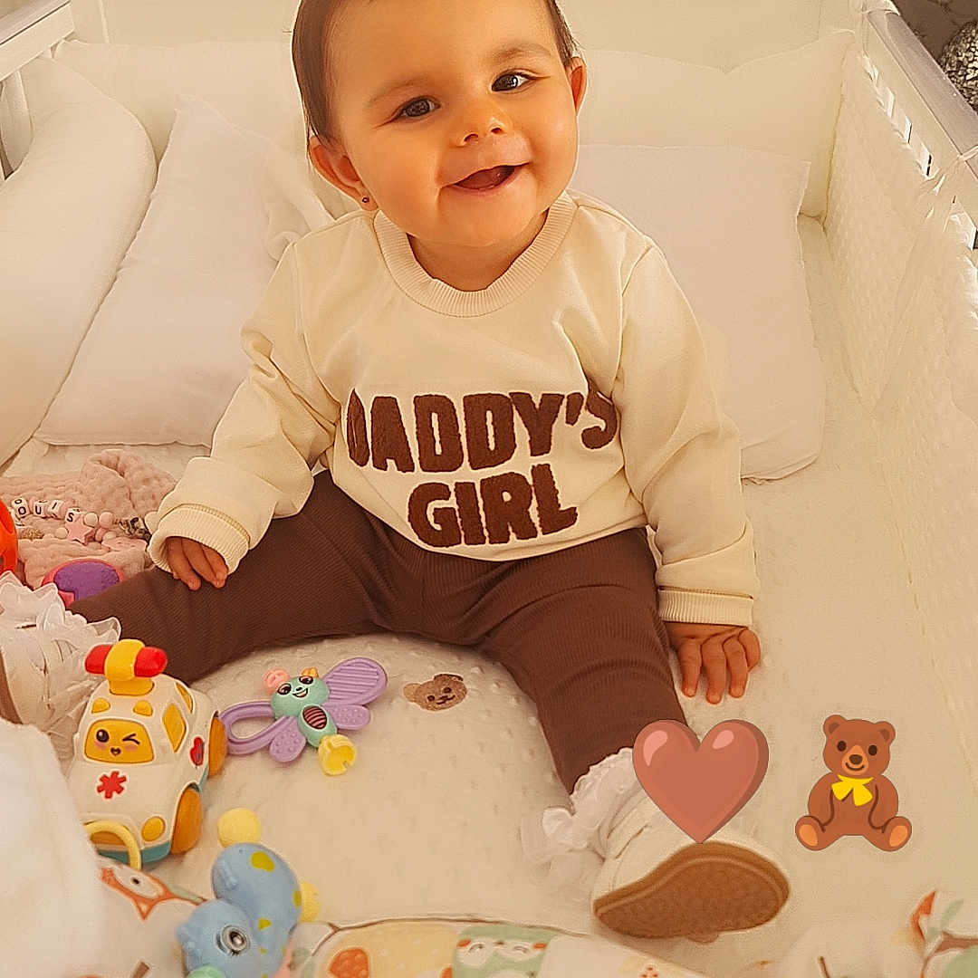Elouise is registered to the contest to win money with this photo: baby, baby_girl, blanket, child, cozy, crib, cute, decor, face, footwear, furniture, happy, indoor, infant, pattern, person, playthings, smile, sweater, toys