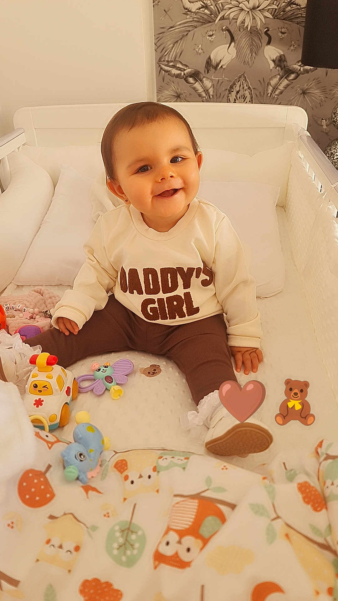 Elouise is registered to the contest to win money with this photo: baby, child, crib, toys, blanket, sweater, smile, happy, indoor, cute, infant, face, person, footwear, decor, pattern, furniture, playthings, baby_girl, cozy