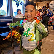 Jr joined the competition — help win amazing prizes! child, toddler, smiling, portrait, restaurant, indoor, stuffed_toy, dinosaur_toy, gold_balloon, birthday, jacket, green_clothing, sportswear, necklace, table, booth, window, diners, background_people, happy