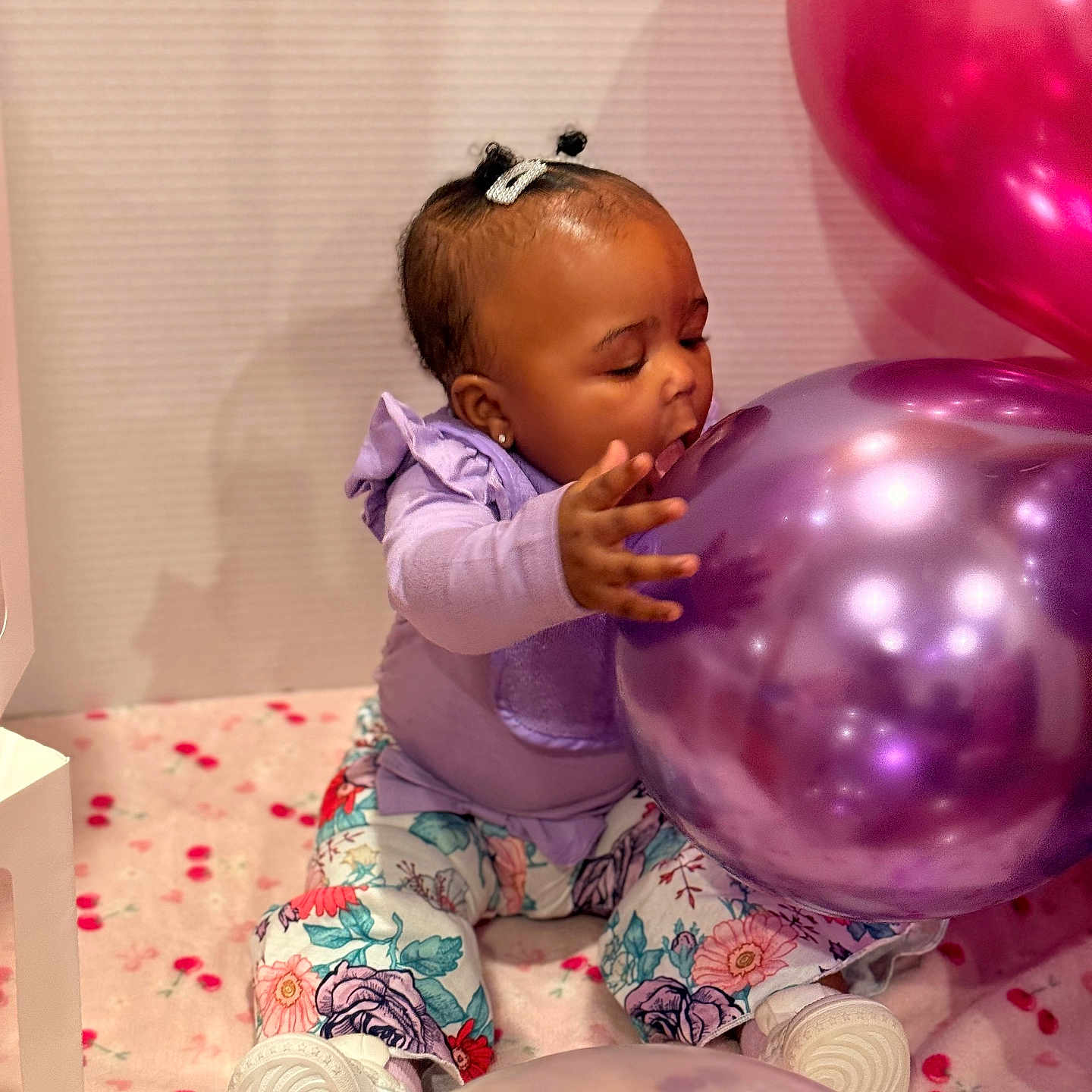Zuri joined the competition — help win amazing prizes! baby, child, infant, sitting, balloons, birthday, party, purple_balloon, pink_balloon, floral_clothing, lavender_shirt, hair_bows, earring, smiling, portrait, indoor, playful, celebration, blanket, colorful