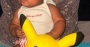 Zuri joined the competition — help win amazing prizes! baby, child, infant, portrait, sitting, pillow, plush_toy, pikachu, toy, yellow, bow, hair_bow, onesie, striped_clothing, smiling, face, indoors, couch, colorful, cute