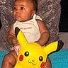 Zuri joined the competition — help win amazing prizes! baby, child, infant, portrait, sitting, pillow, plush_toy, pikachu, toy, yellow, bow, hair_bow, onesie, striped_clothing, smiling, face, indoors, couch, colorful, cute