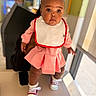 Zuri joined the competition — help win amazing prizes! baby, infant, child, portrait, standing, indoors, pink_outfit, dress, bib, bow_headband, red_sneakers, shoes, smiling, looking_at_camera, dark_skin, window, daylight, chair, home, fashion