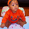 Zuri is registered to the contest to win money with this photo: baby, bed, blanket, child, colorful, earrings, eyes, face, halloween, hat, indoor, infant, orange_outfit, photography, portrait, pumpkin_costume, shoes, sitting, smiling, white_shoes