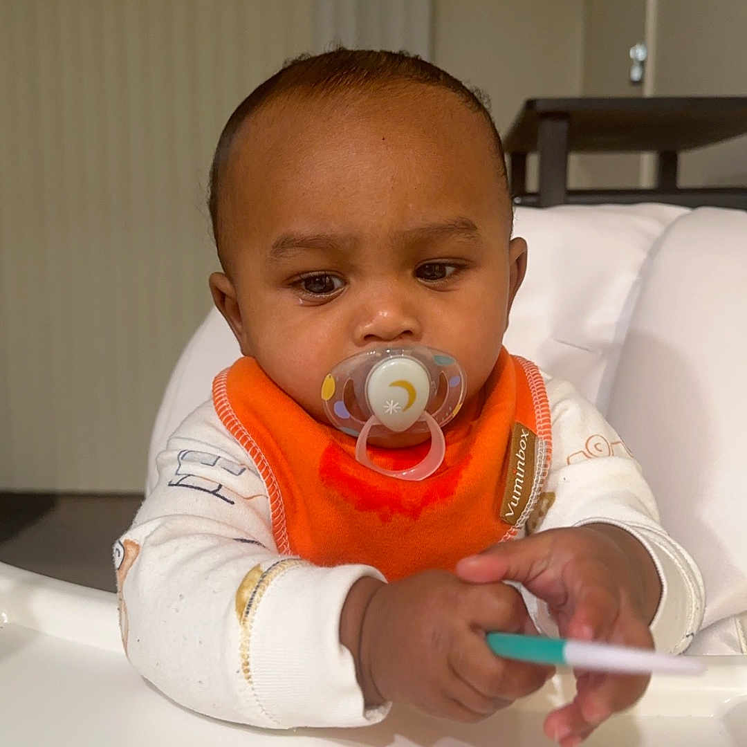 Orion is registered to the contest to win money with this photo: baby, bodypart, cream, cutlery, dessert, face, finger, food, furniture, hand, head, icecream, mouth, person, photography, portrait, sitting, spoon, table, teeth