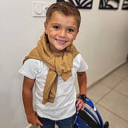 Gabriel participe au concours pour gagner de l'argent avec cette photo : child, boy, smiling, indoor, white_tshirt, tan_sweater, backpack, shorts, shoes, tile_floor, modern_art, hair, person, portrait, happy, standing, hand, young, casual_clothing, wall