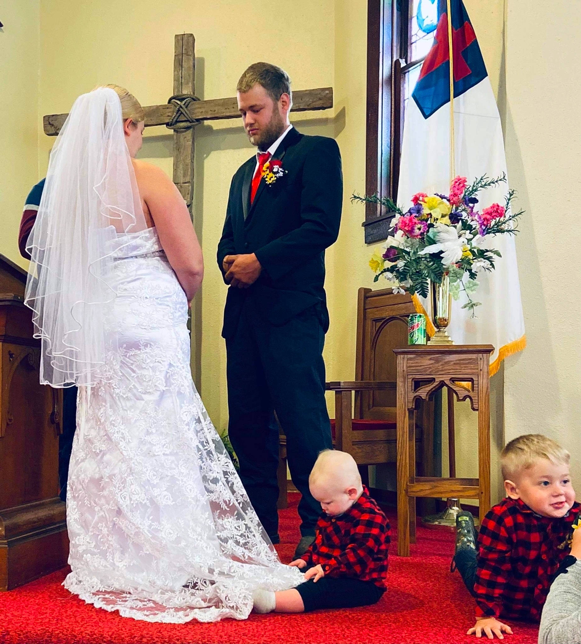 Colton is registered to the contest to win money with this photo: bridal_clothing, bridal_veil, bride, flag, flower, flower_arranging, formal_wear, gesture, gown, happy, interaction, person, photograph, rite, standing, suit, tie, toddler, veil, wedding_ceremony_supply