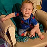 toddler, child, baby, sitting, smiling, portrait, face, indoor, armchair, chair, cushion, blanket, clothing, superhero_costume, blue_shirt, barefoot, living_room, furniture, happy, photography