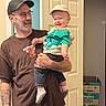 man, baby, child, indoor, smiling, cap, glasses, tshirt, jeans, socks, tattoo, door, box, diapers, happy, holding, person, family, casual, home