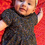 Brianna participe au concours pour gagner de l'argent avec cette photo : baby, child, smiling, headband, floral_pattern, dress, fabric, blanket, red, pattern, cute, portrait, infant, happy, laying_down, skin, face, person, indoors, closeup