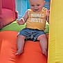 James is registered to the contest to win money with this photo: baby, child, smiling, yellow_shirt, denim_shorts, inflatable_slide, orange, green, blue, yellow, outdoor, sunlight, happy, play, summer, fun, person, toddler, cute, clothing