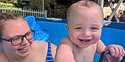 James joined the competition — help win amazing prizes! baby, child, woman, glasses, pool, inflatable_pool, water, smile, happy, outdoor, summer, play, hand, face, blue, green, striped_clothing, person, backyard, fun