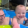 baby, child, woman, glasses, pool, inflatable_pool, water, smile, happy, outdoor, summer, play, hand, face, blue, green, striped_clothing, person, backyard, fun