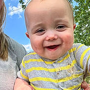James is registered to the contest to win money with this photo: baby, child, smiling, happy, outdoor, sky, tree, greenery, onesie, striped_clothing, person, face, hand, holding, cute, infant, daylight, casual, portrait, nature
