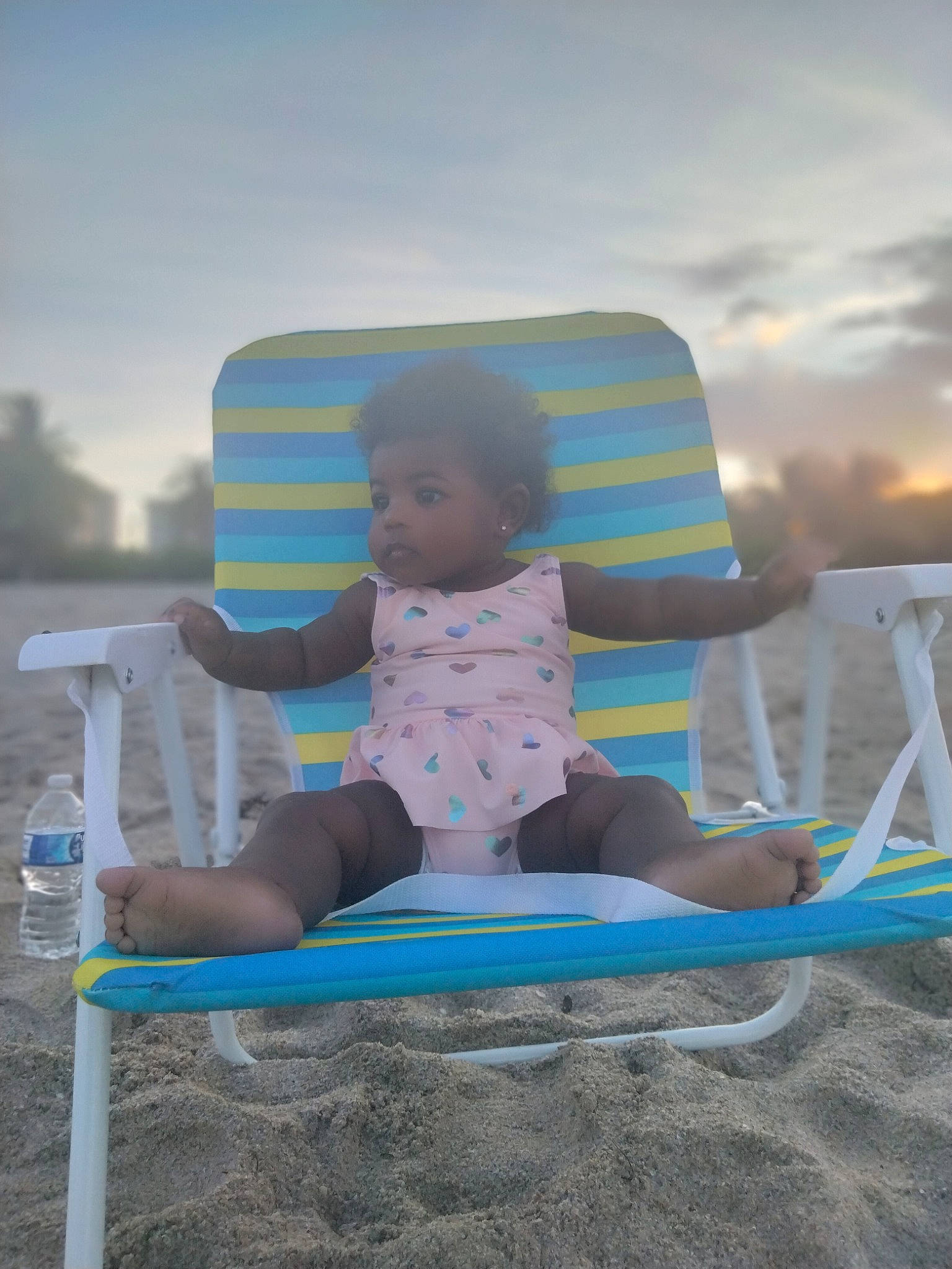 Wynter is registered to the contest to win money with this photo: baby, baby_toddler_clothing, beach, body_of_water, chair, cloud, comfort, fun, horizon, leisure, outdoor_furniture, person, recreation, sand, shade, shorts, sitting, sky, t_shirt, toddler
