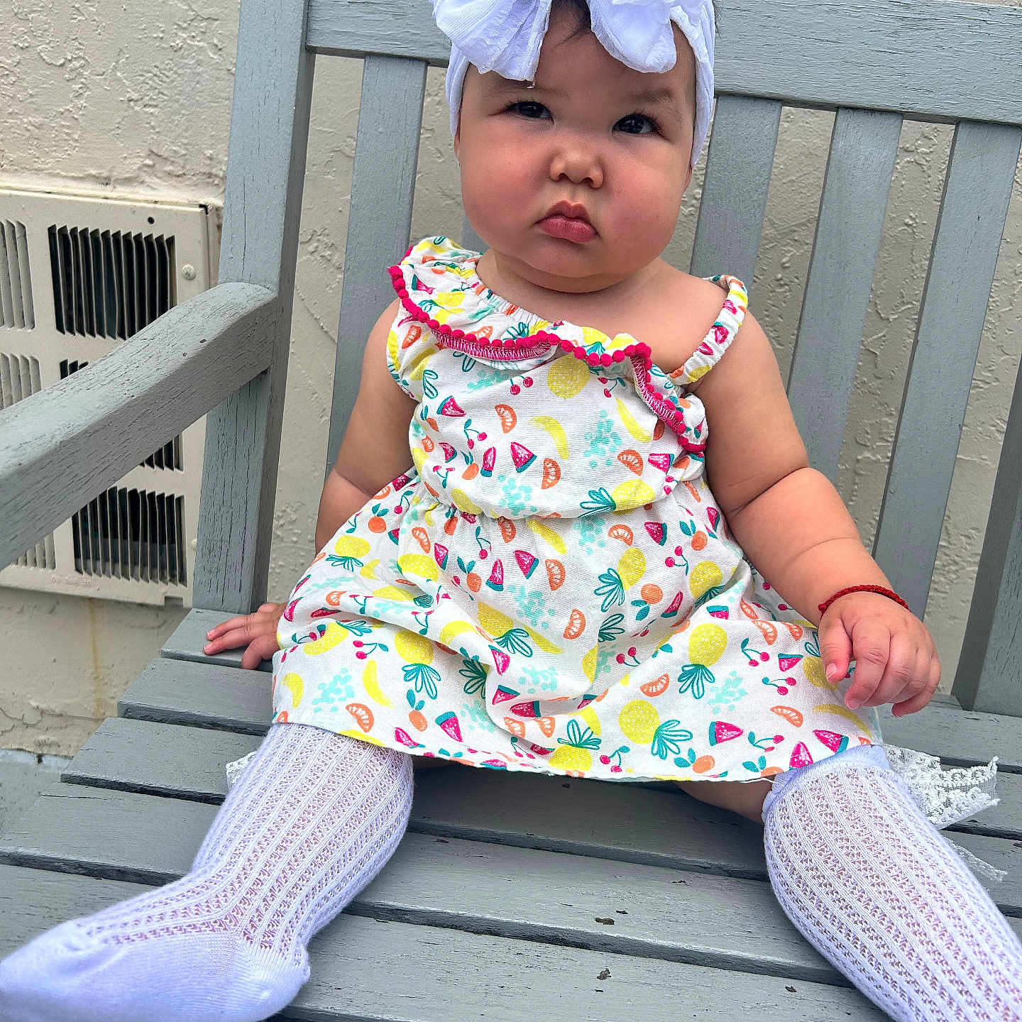 Alysson is registered to the contest to win money with this photo: baby, child, girl, bench, headband, white_bow, colorful_dress, fruit_pattern, knit_socks, outdoor, wooden_bench, serious_expression, person, sitting, cute, infant, plush, fashion, portrait, skin