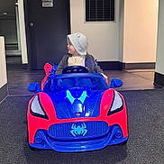 Noah Bautista is registered to the contest to win money with this photo: blue, car, carpet, child, clothing, curious, door, floor, flooring, hat, headwear, indoor, looking_sideways, person, play, red, toddler, toy_car, vehicle, vent
