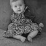 baby, child, infant, leopard_print, dress, sitting, carpet, cute, portrait, indoor, face, smiling, person, clothing, long_sleeve, barefoot, young, expression, curly_hair, black_and_white