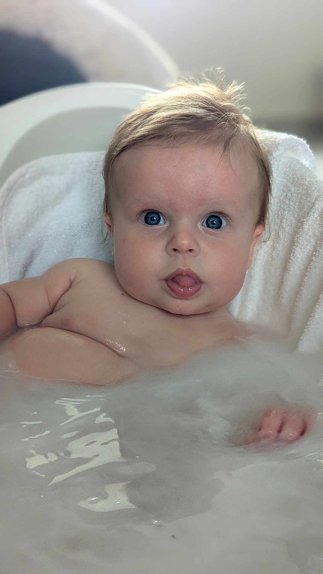 Violet is registered to the contest to win money with this photo: baby, bath, water, bubbles, towel, blue_eyes, tongue, skin, child, cute, infant, playful, wet, face, head, person, indoors, relaxing, young, expression