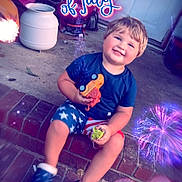 Logan joined the competition — help win amazing prizes! child, toddler, smiling, toy, brick_steps, blue_shirt, shorts, sneakers, fireworks, holiday, celebration, text_overlay, patriotic, 4th_of_july, outdoor, door, concrete_floor, playful, festive, happy