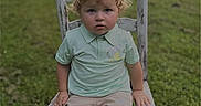 Logan joined the competition — help win amazing prizes! blonde, boy, chair, child, curly_hair, daylight, field, green_grass, nature, outdoor, person, polo_shirt, portrait, rustic, serious_expression, shorts, sitting, summer, toddler, wooden_chair