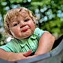 Logan is registered to the contest to win money with this photo: toddler, child, face, portrait, expression, pout, curly_hair, blonde, green_shirt, outdoor, nature, bokeh, playful, cute, person, young_child, smile, daylight, happy, closeup