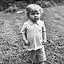 Logan is registered to the contest to win money with this photo: child, toddler, boy, barefoot, grass, outdoor, polo_shirt, shorts, curly_hair, black_and_white, portrait, serious, standing, nature, young_child, casual_clothing, daylight, expression, lawn, alone