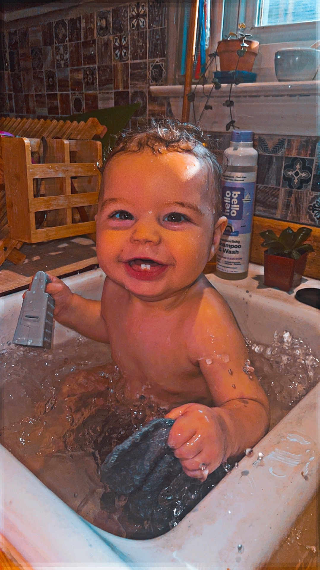 Weston is registered to the contest to win money with this photo: baby, bath, sink, water, splash, smile, happy, child, toy, kitchen, plant, shampoo, tiled_wall, wet, infant, hand, face, cute, indoor, playful