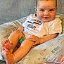 Weston is registered to the contest to win money with this photo: baby, child, infant, smile, cushion, clothing, foot, hand, face, indoor, cute, sitting, pattern, text, fabric, comfort, skin, happy, portrait, toddler