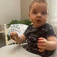 Weston is registered to the contest to win money with this photo: toddler, high_chair, messy_face, food, eating, indoor, child, plate, hand, chair, table, curtain, plant, shirt, face, expression, dining_room, baby, meal, home