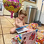 baby, child, birthday, balloon, toy, kitchen, floor, box, wrapping_paper, tiled_floor, curious, indoors, happy_birthday, unwrapped_gift, diaper, candid, young_child, smile, play, present