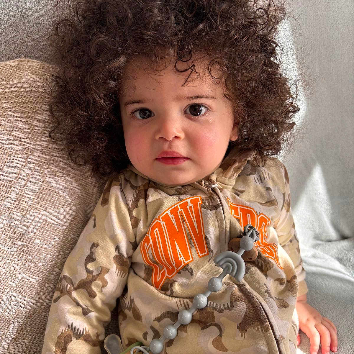 Liam participe au concours pour gagner de l'argent avec cette photo : baby, blanket, casual, child, clothing, couch, cozy, curly_hair, cute, dinosaur_print, expression, eyes, face, indoor, pacifier_clip, portrait, sitting, soft_lighting, toddler, young_child