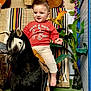 toddler, child, goat, indoor, plant, sweatshirt, red_clothing, barefoot, decor, guitar, woven_textile, smiling, animal, furniture, colorful, happy, portrait, baby, cute, pet
