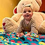 baby, child, smile, teddy_bear, plush_toy, blanket, colorful, indoor, floor, cute, happy, sitting, toy, warm_lighting, young_child, clothing, playful, infant, cozy, portrait