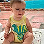 baby, child, onesie, yellow_clothing, fish_design, smiling, outdoor, courtyard, building, stairs, white_chair, skin, person, happy, sitting, daylight, plush, cute, infant, casual