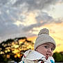 baby, child, hat, knit_hat, hoodie, donald_duck, sunset, outdoor, sky, clouds, grass, playful, cute, portrait, childhood, expression, nature, warm_clothing, smiling, face