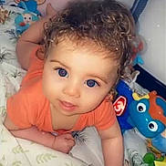 Menzo participe au concours pour gagner de l'argent avec cette photo : baby, child, curly_hair, blue_eyes, toys, minnie_mouse, pillow, bed, blanket, orange_shirt, infant, cute, indoor, playful, person, smiling, lying_down, colorful, soft, closeup