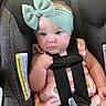 baby, infant, car_seat, headband, bow, pink_clothing, fruit_print, straps, safety_harness, plush_toy, blue_eyes, rosy_cheeks, cute, child, seat, indoor, portrait, closeup, person, toddler