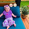 baby, blue_cushion, child, cute, face, floral_pants, grass, headband, infant, milestone_plaques, my_first_easter, outdoor, portrait, potted_plant, purple_clothing, seven_months, sitting, smiling, wooden_deck, wooden_fence