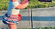 Clair-Ann is registered to the contest to win money with this photo: baby, blue, brick_wall, building, car, child, curious, flag, grass, happy, headwrap, outdoor, patriotic, red, sidewalk, skirt, standing, sunlight, white, window