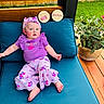 baby, barefoot, child, cushion, cute, daylight, floral_pattern, greenery, headband, infant, milestone_sign, outdoor, plant, portrait, purple_clothing, relaxing, seven_months, sitting, smiling, wooden_deck