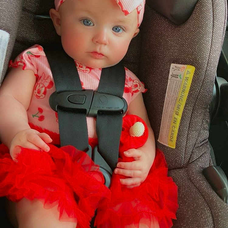 Clair-Ann is registered to the contest to win money with this photo: baby, child, car_seat, red_tutu, headband, blue_eyes, sitting, safety_harness, cute, infant, clothing, sock, indoor, portrait, seat_belt, pink, red, person, young_child, car_interior