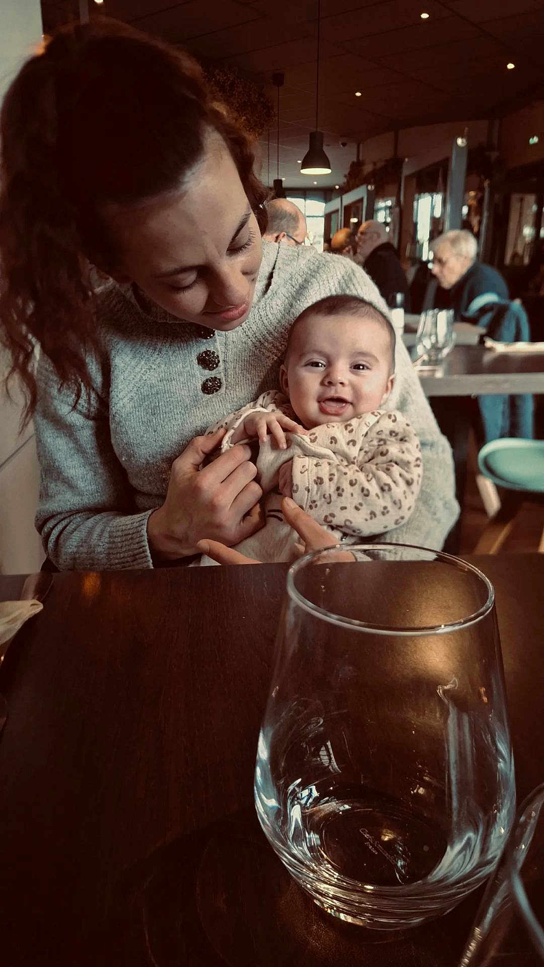 Agathe participe au concours pour gagner de l'argent avec cette photo : baby, woman, smile, cafe, indoor, table, glass, sweater, holding, people, restaurant, happy, portrait, seated, leopard_print, warm_lighting, background, face, person, love