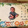 baby, infant, milestone_blanket, cartoon_animals, elephant, tiger, zebra, lion, monkey, giraffe, numbers, months, greenery, heart_shape, smiling, clothing, floor, carpet, cute, celebration